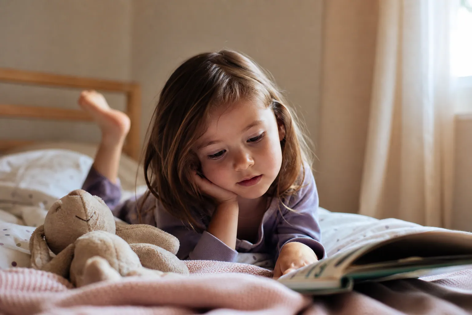 Un jeune enfant allongé sur son lit regarde un livre d'images dans une chambre baignée de lumière douce