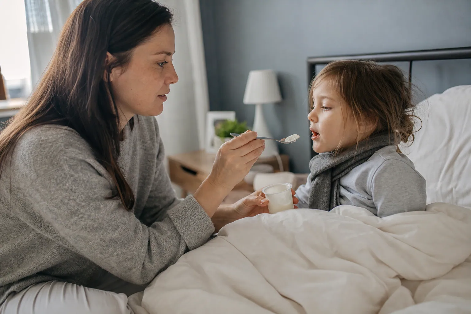 Un parent apporte un yaourt à un enfant malade assis dans son lit.
