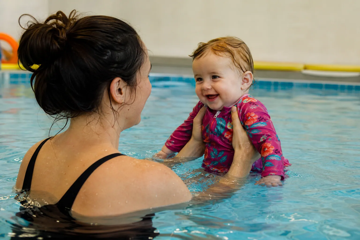 Un parent tient son bébé dans l'eau d'une piscine chauffée lors d'une séance de bébé nageur.
