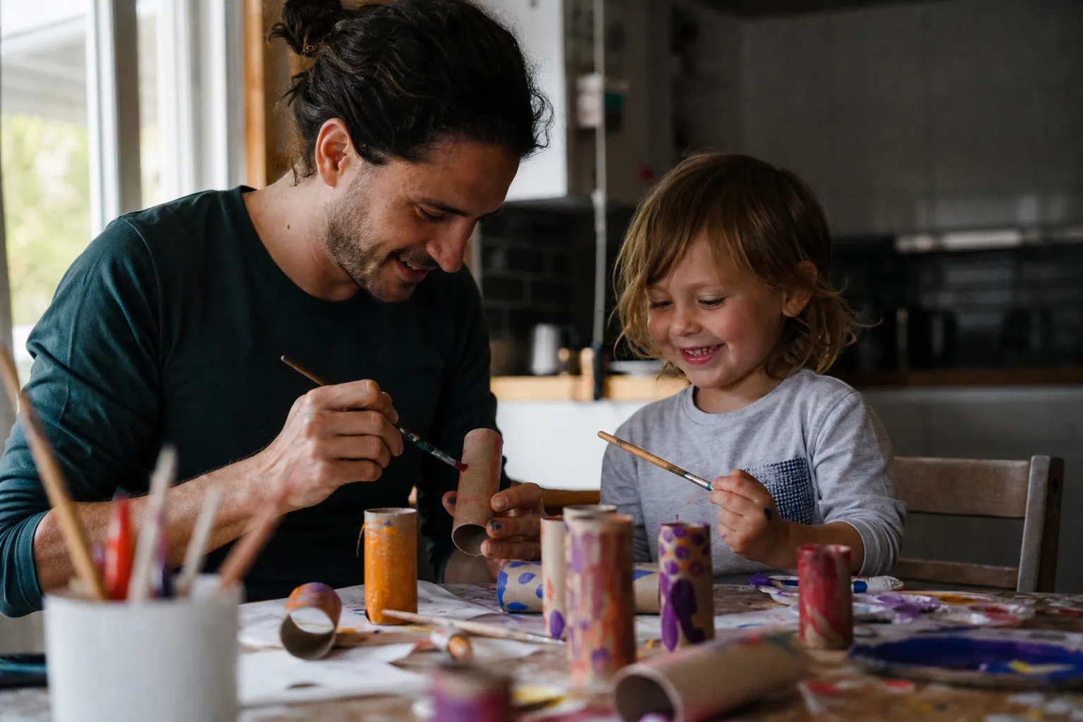 Parent et enfant bricolant ensemble avec des rouleaux de papier toilette peints sur une table
