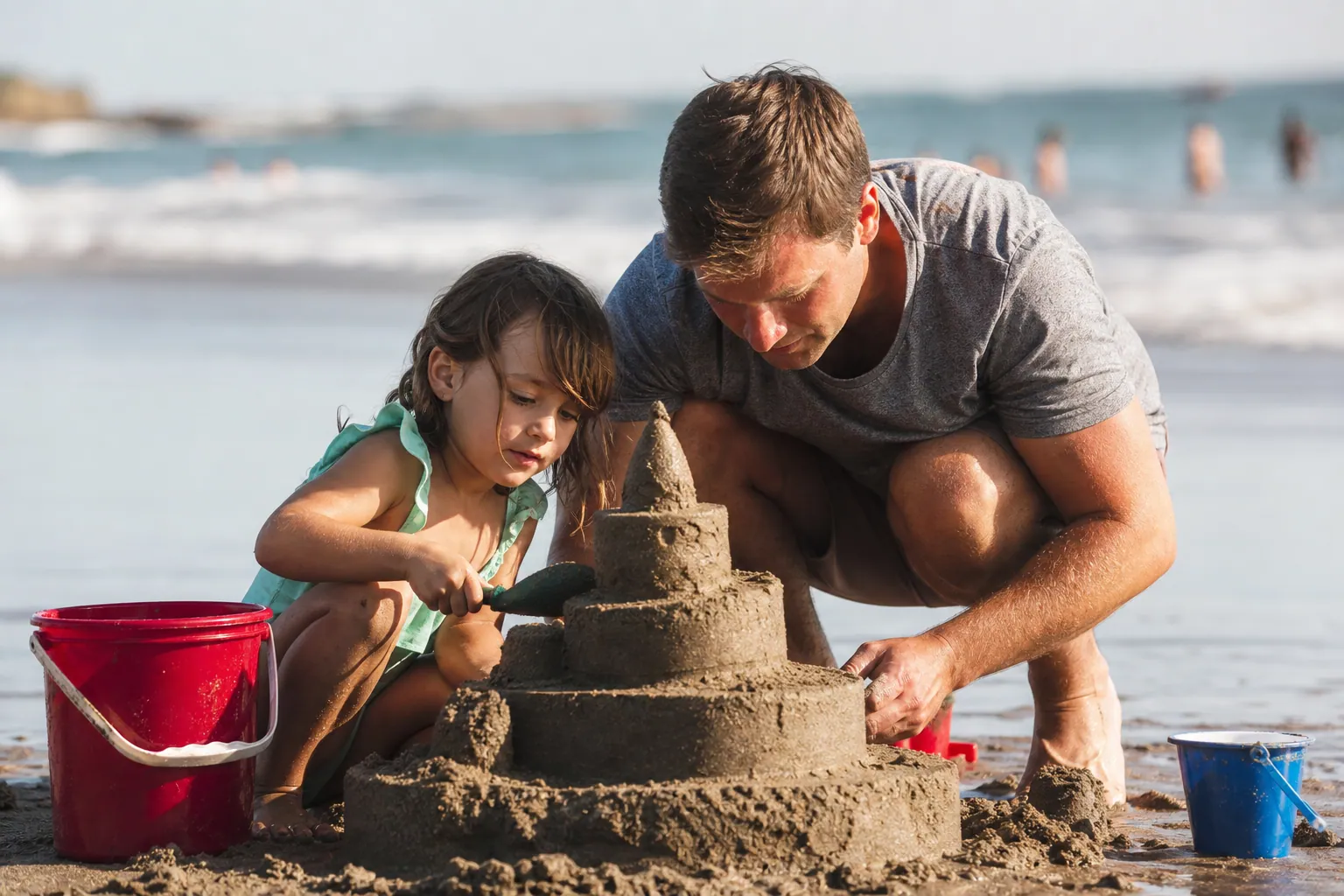 Un enfant et son père construisent ensemble une tour de sable sur la plage.