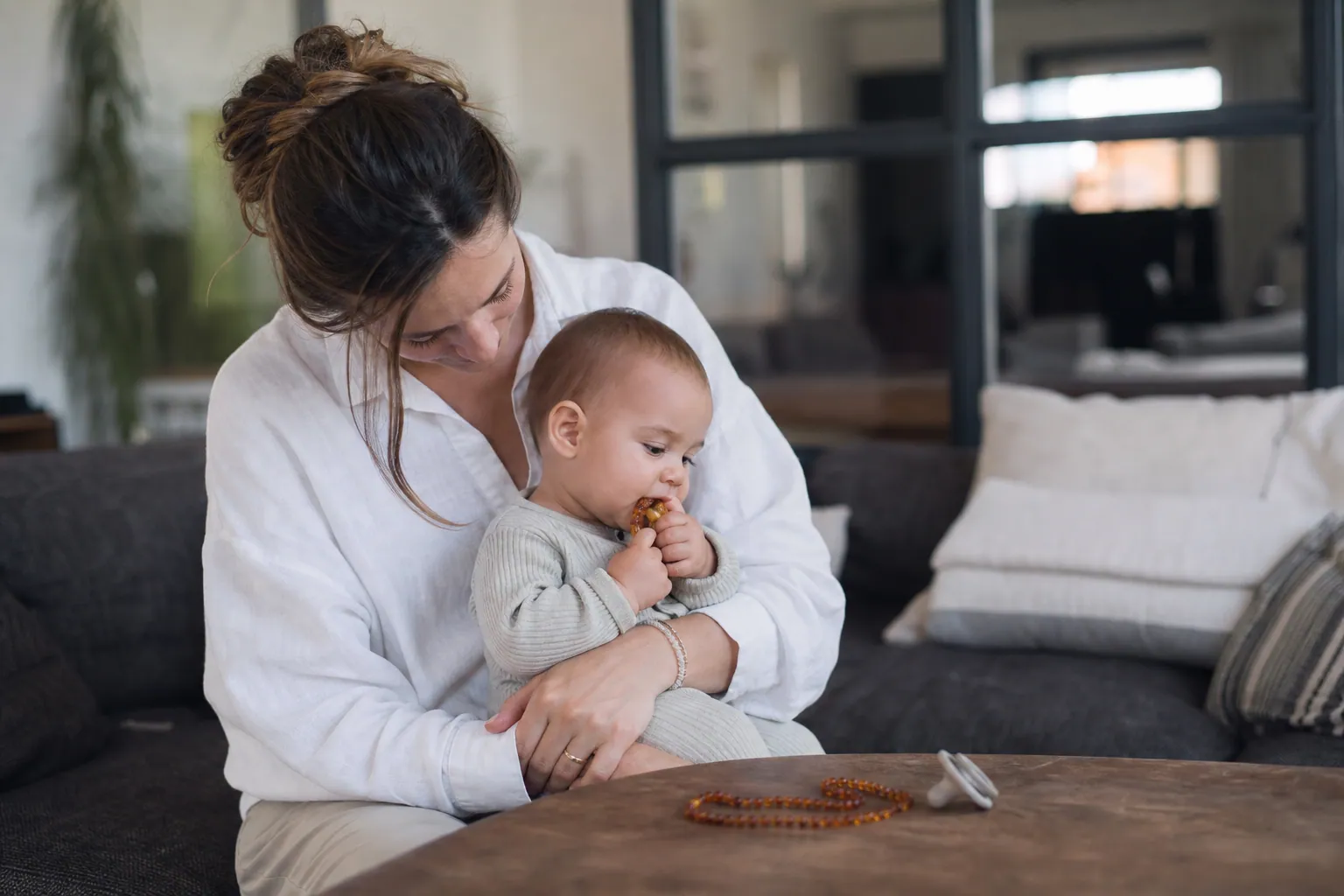 Parent avec bébé et collier d’ambre posé près d’un anneau de dentition.