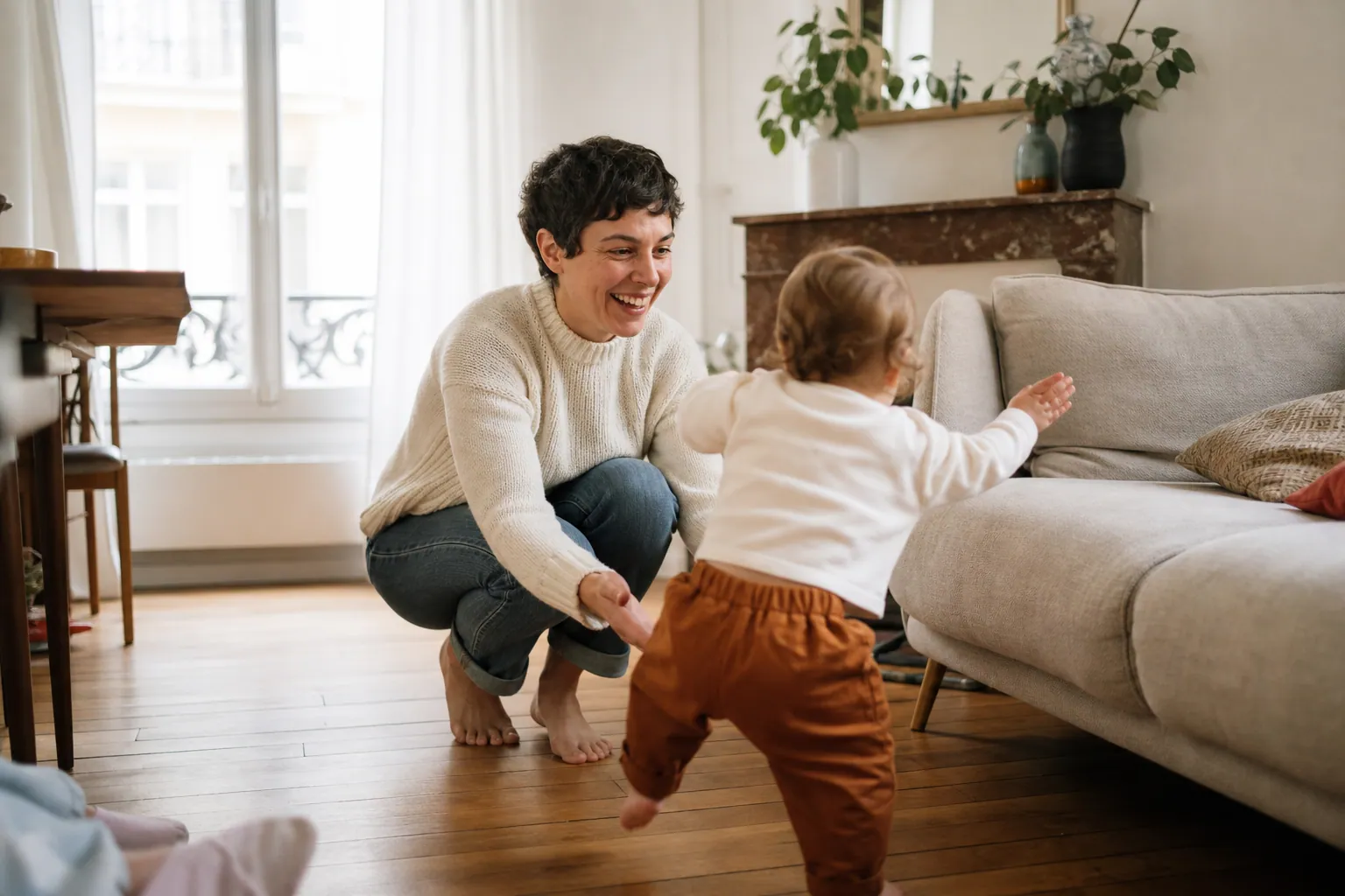 Parent encourageant un tout-petit à faire ses premiers pas dans le salon.