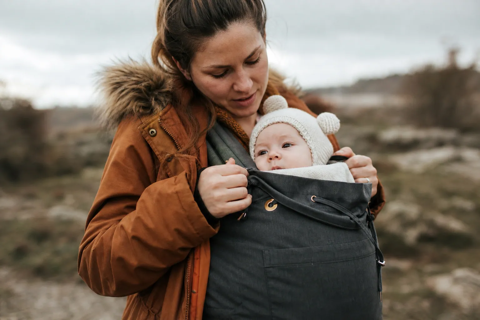 Parent ajustant une couverture de portage sur un bébé contre sa poitrine