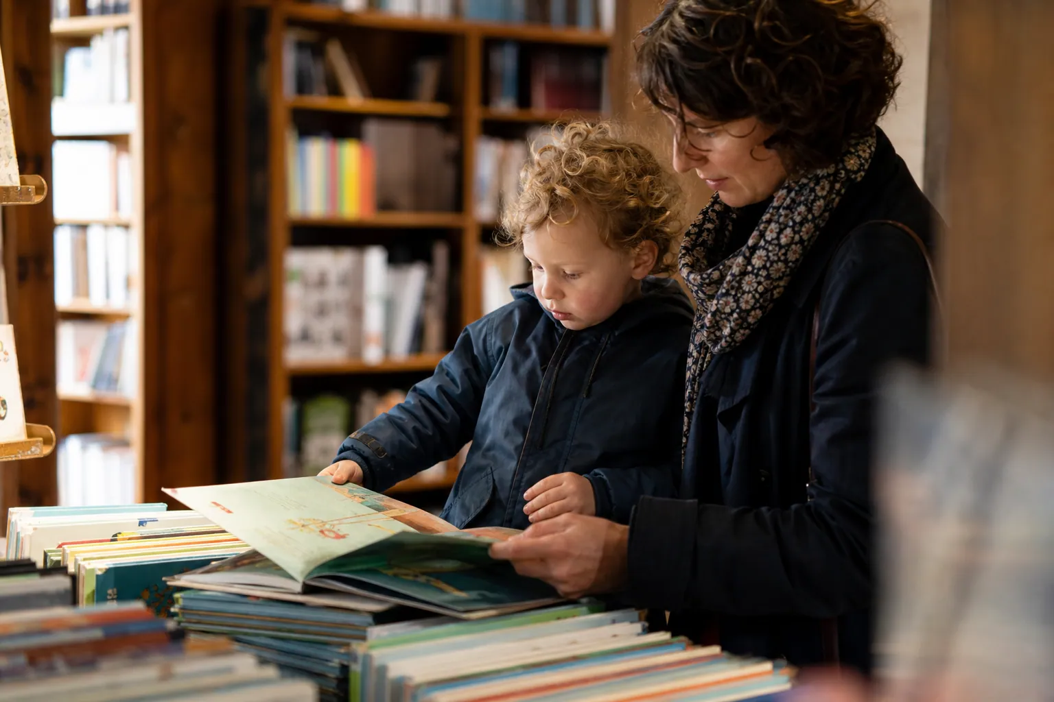 Parent et enfant feuilletant des livres jeunesse dans une librairie lumineuse