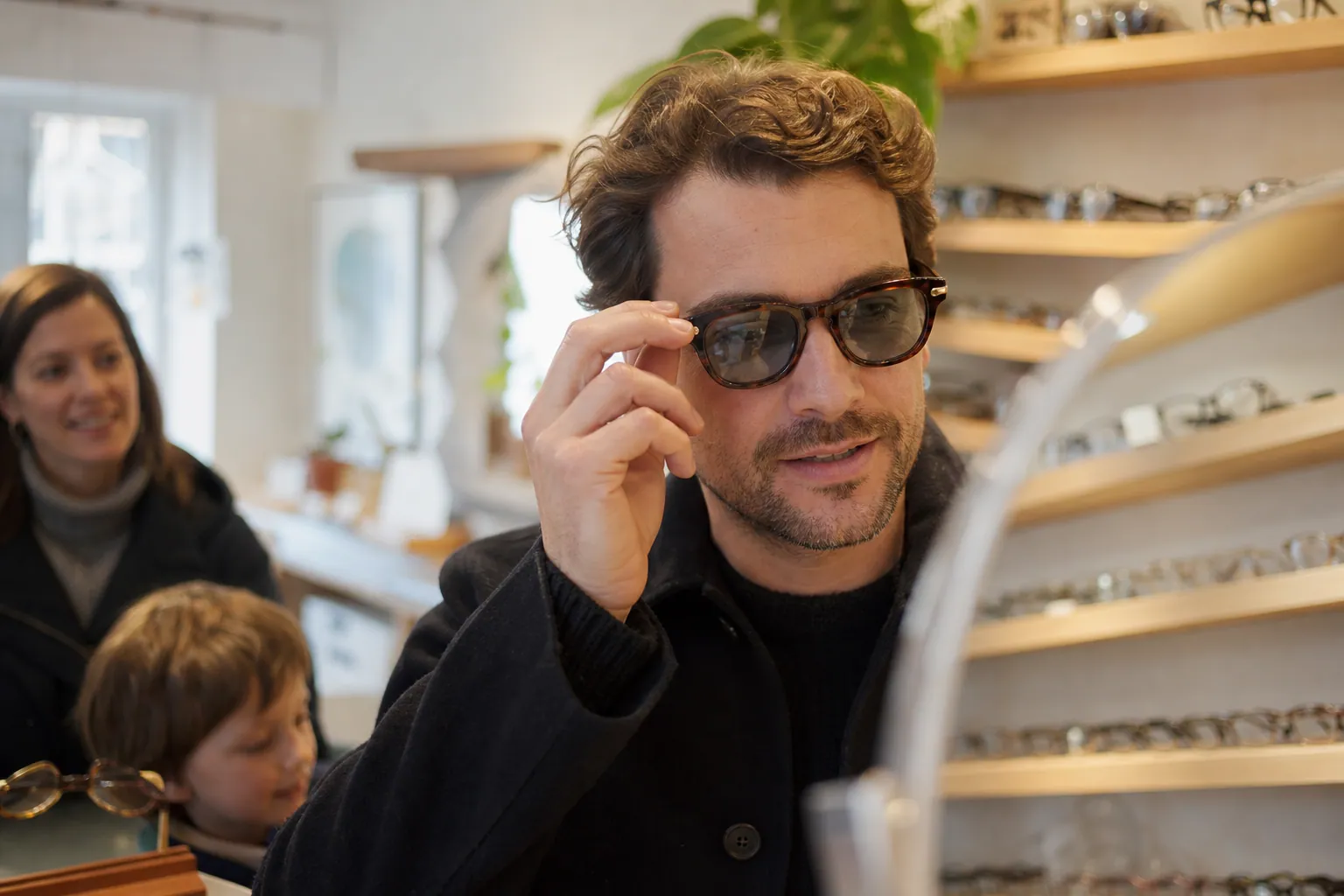 Personne essayant plusieurs lunettes Persol devant un miroir, dans une boutique lumineuse et chaleureuse.