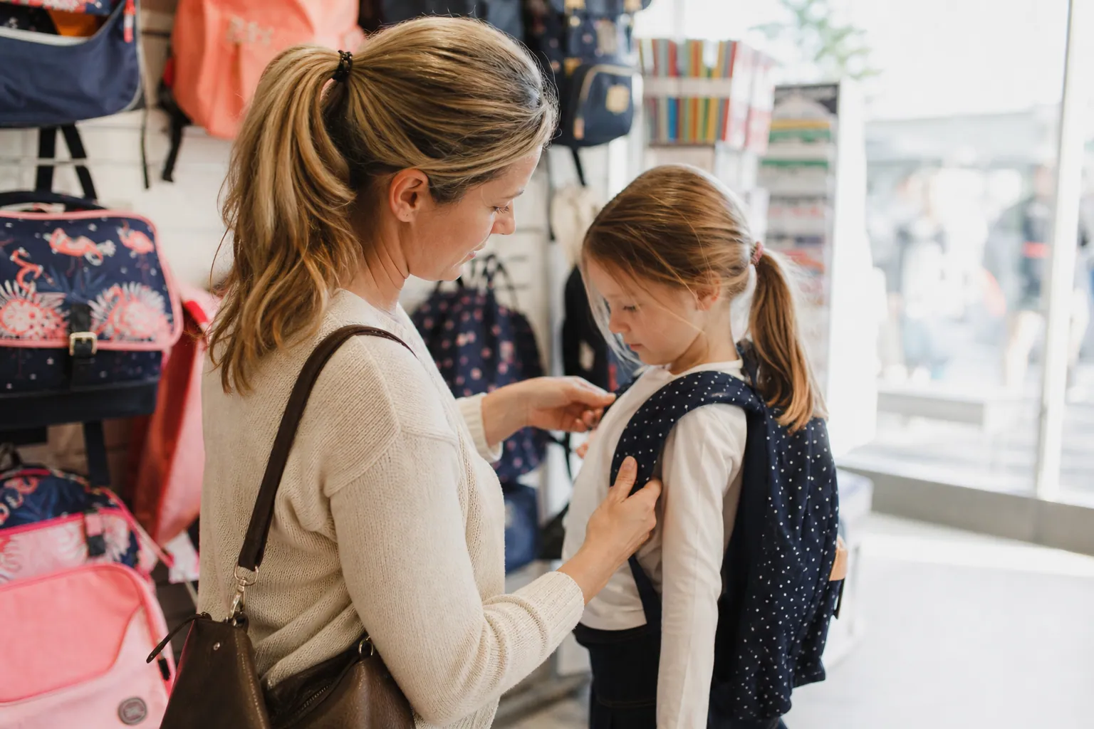 Parent aidant son enfant à essayer un cartable en magasin avant la rentrée