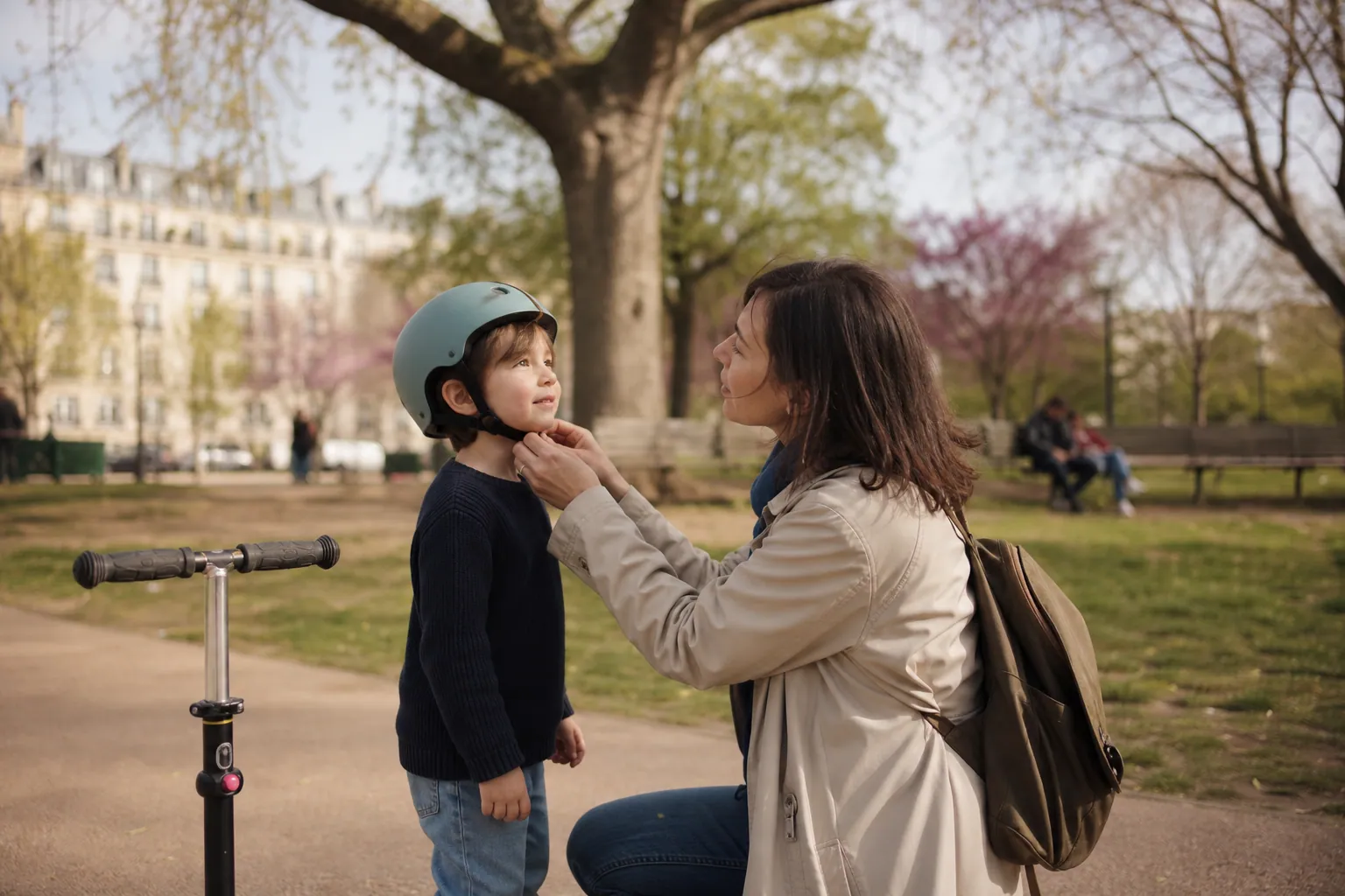 Parent aidant un enfant à enfiler un casque avant de monter sur sa trottinette dans un parc.