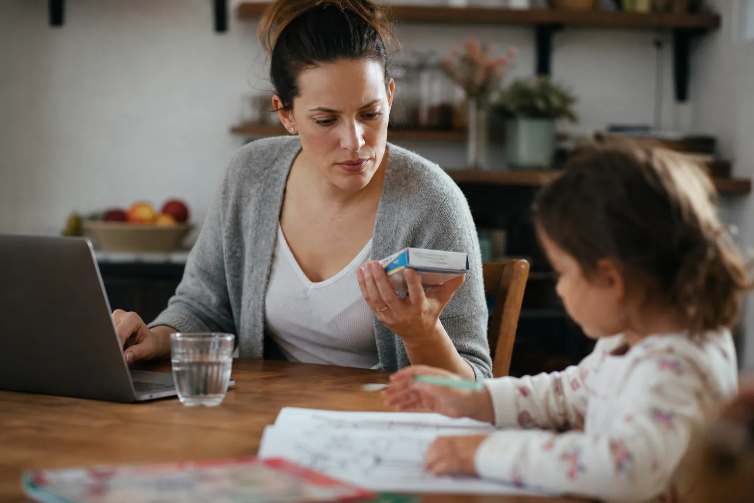 Parent consultant la notice d’un médicament sur ordinateur, avec une boîte à côté.