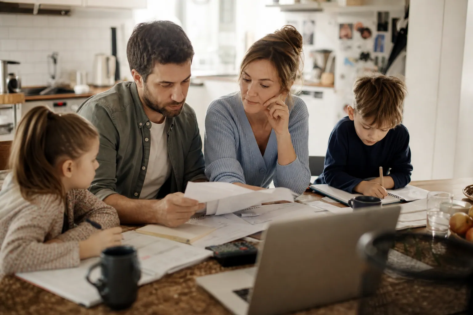 Parents français à table, calculatrice et carnet, en train de préparer le budget familial.