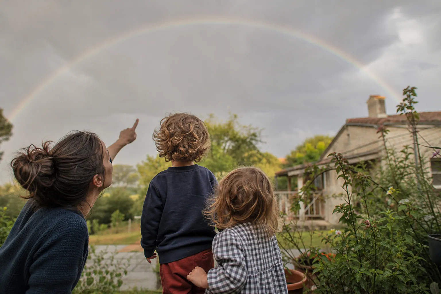 Parent et enfants montrant un arc-en-ciel dans le ciel après la pluie.
