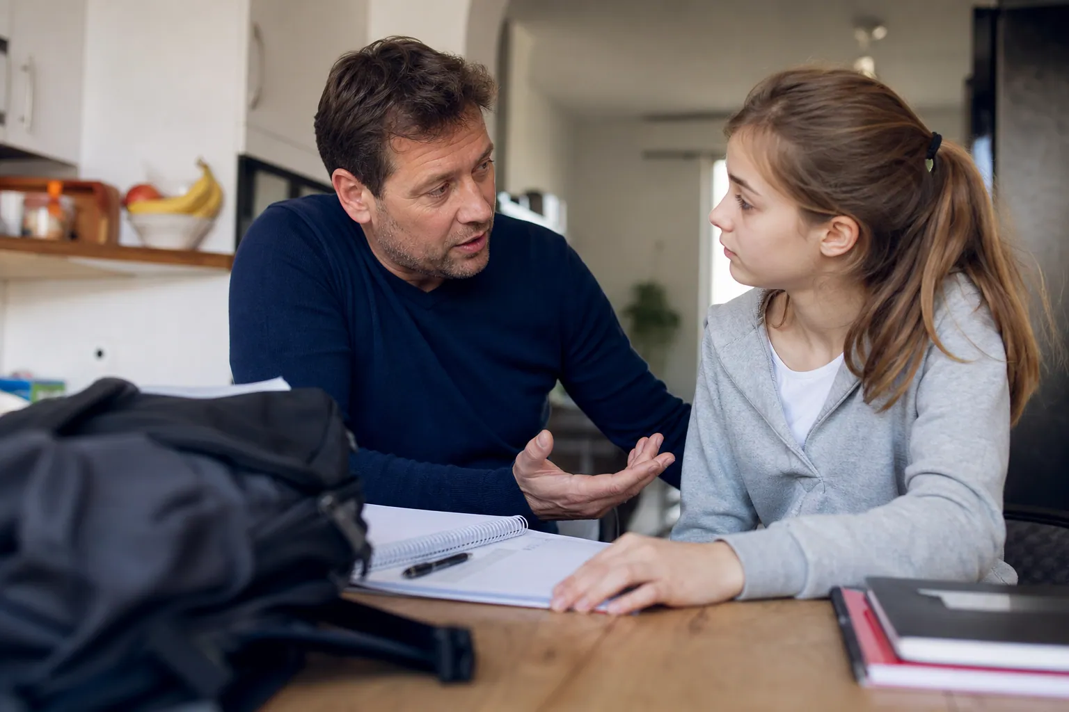 Parent discutant calmement avec son adolescent autour des devoirs à la maison.