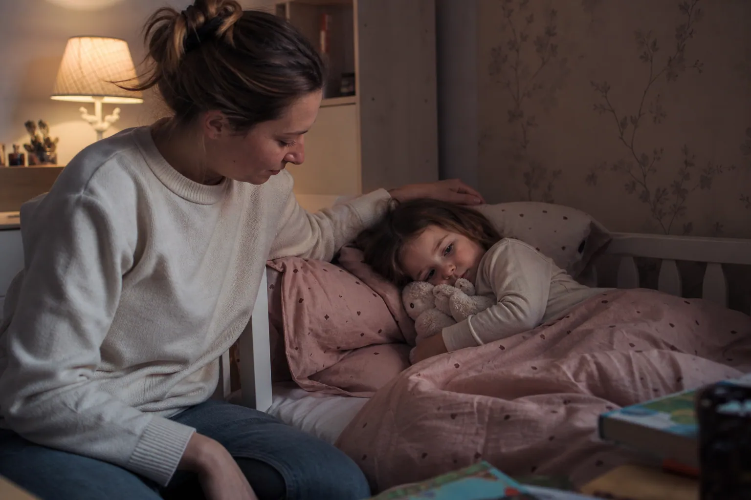Parent rassurant son enfant au coucher dans une chambre chaleureuse et calme.