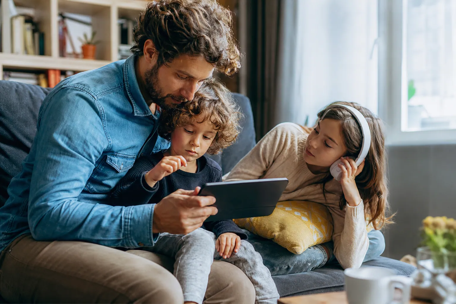 Parent et enfant choisissant de la musique en ligne sur une tablette, dans un salon lumineux.