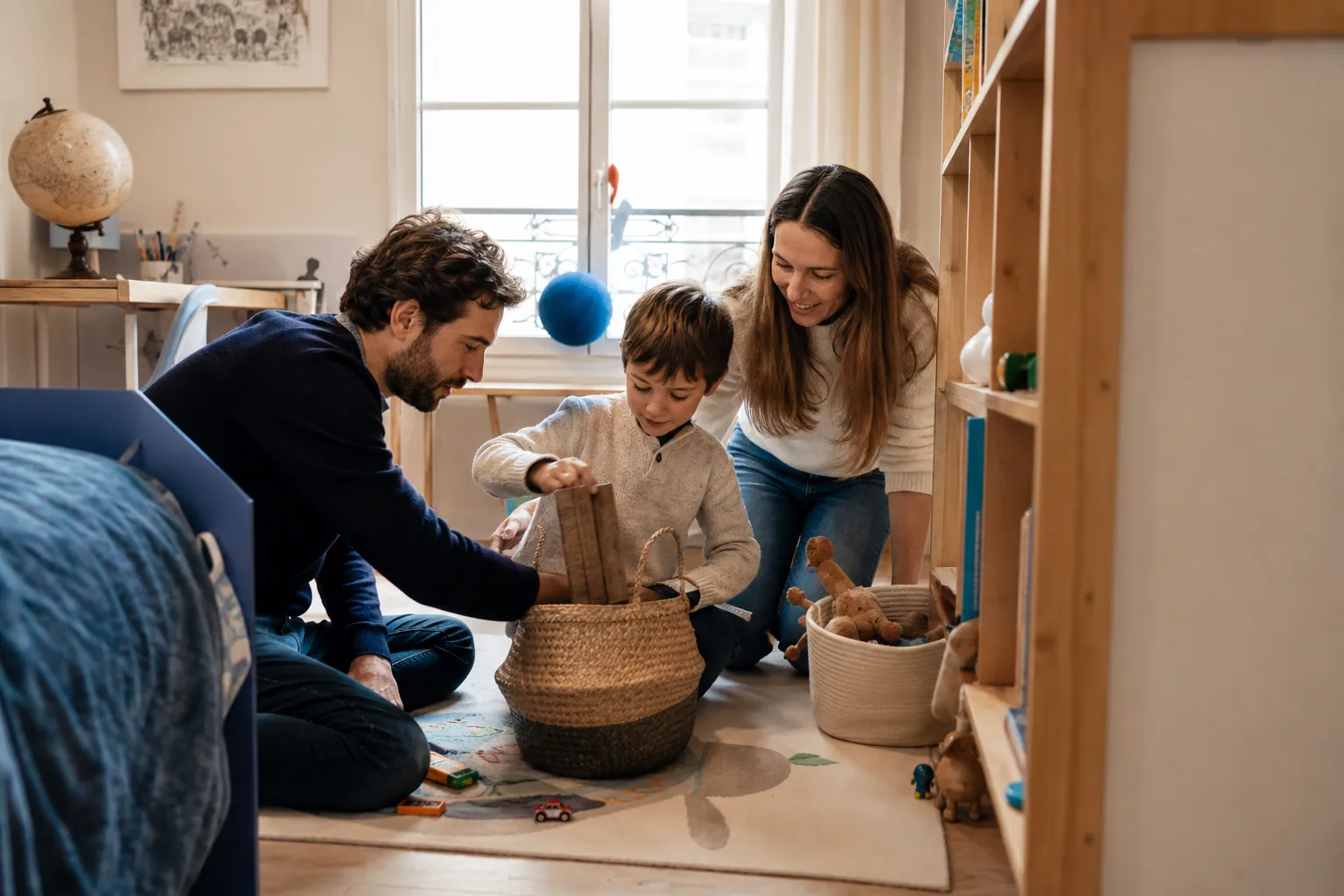 Parents et enfant rangeant ensemble une chambre de garçon lumineuse et bien organisée.