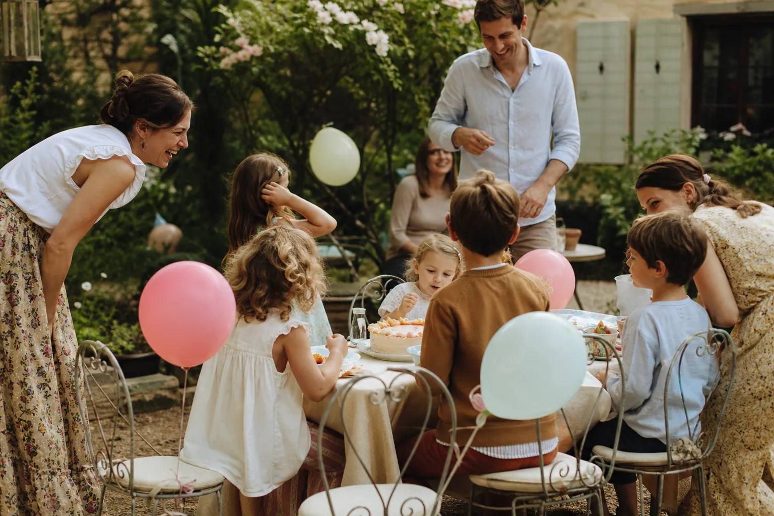 Anniversaire d’enfant en extérieur dans un jardin, avec enfants, parents, gâteau et décor simple.