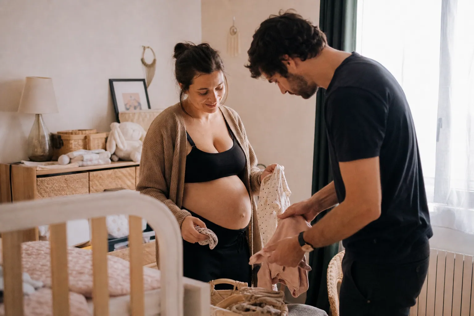 Parents préparant une chambre simple et chaleureuse pour l’arrivée de bébé.