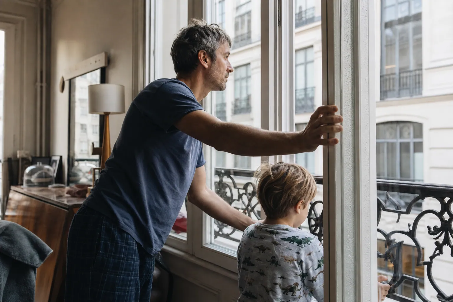 Parent aérant une fenêtre en aluminium avec de la buée, dans un intérieur familial chaleureux.