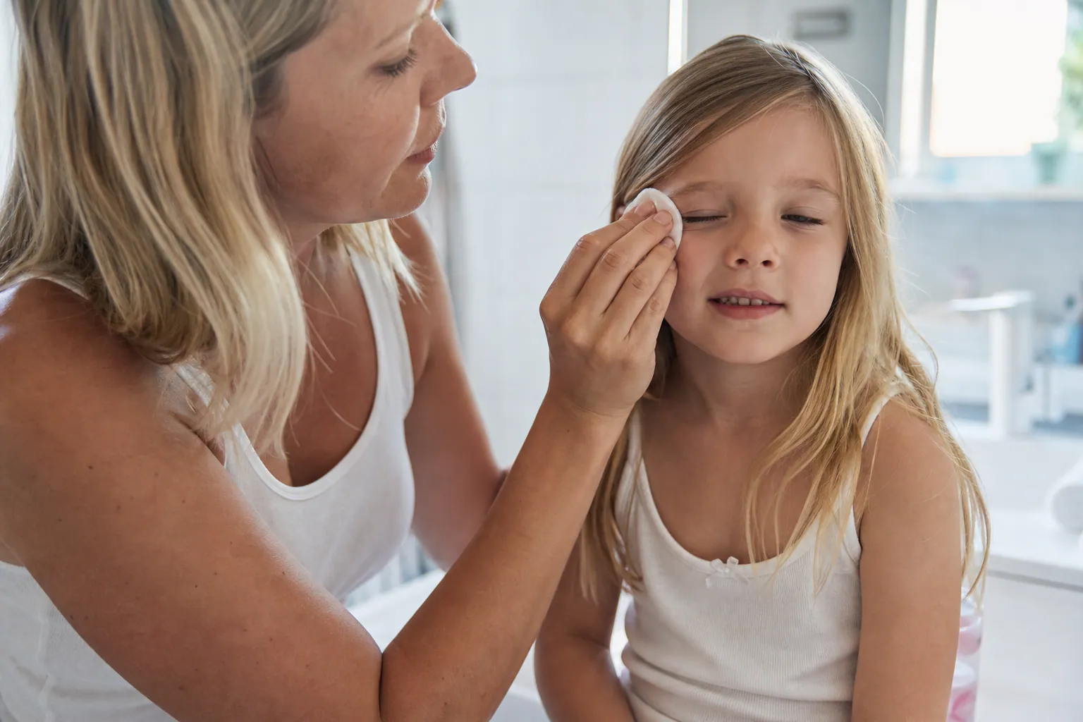 Un parent nettoie délicatement l'œil de son enfant avec une compresse douce.