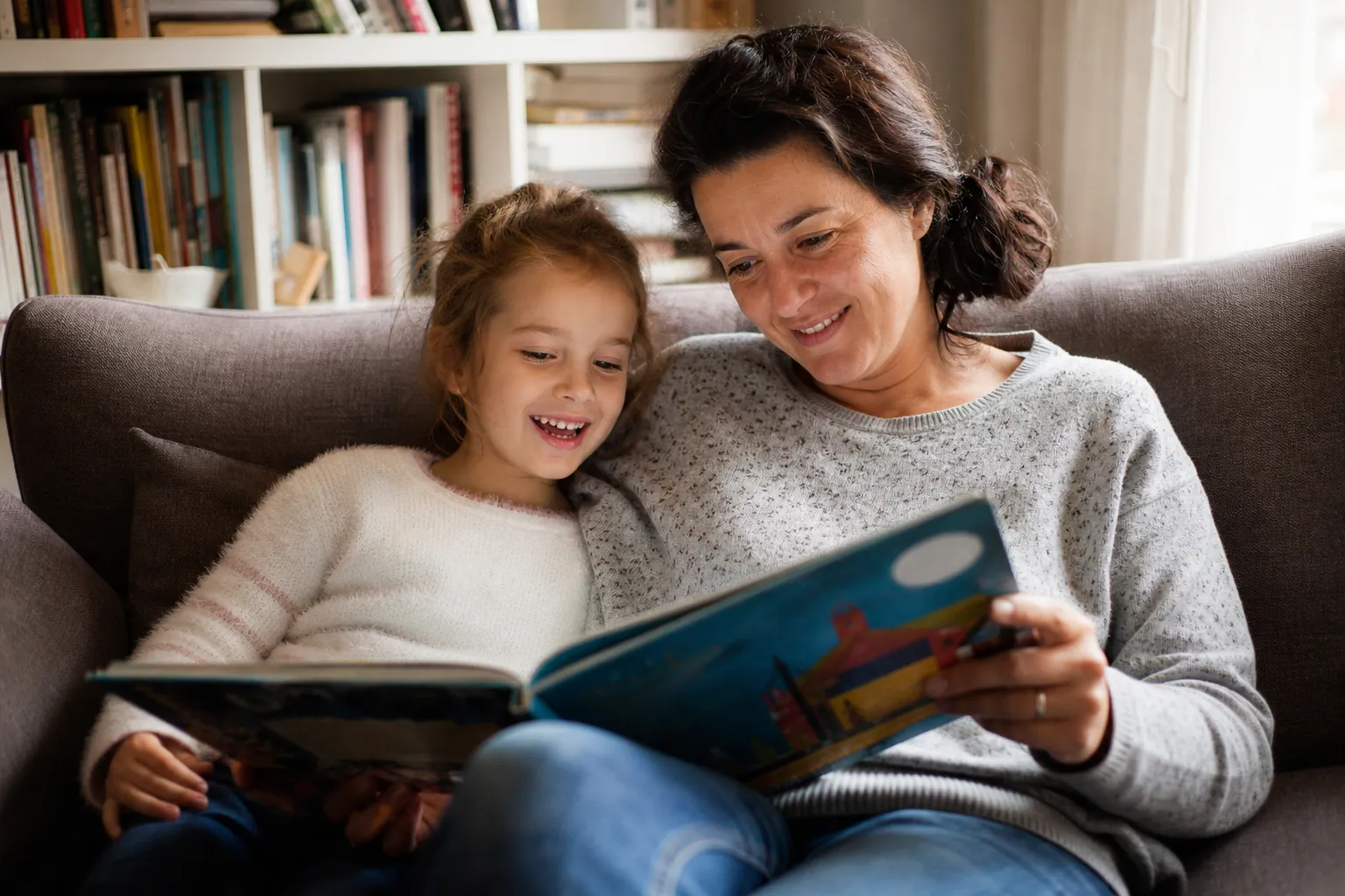 Parent lisant un livre avec son enfant dans un salon lumineux et chaleureux.