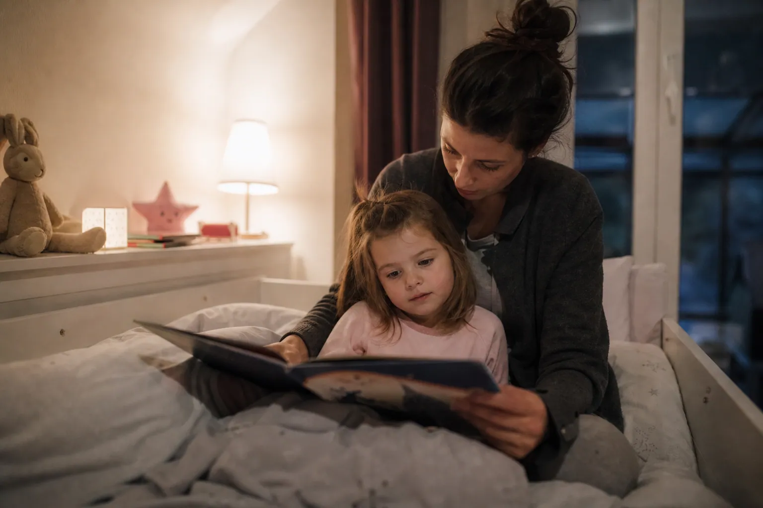 Parent lisant une histoire à son enfant au moment du coucher dans une chambre apaisante.