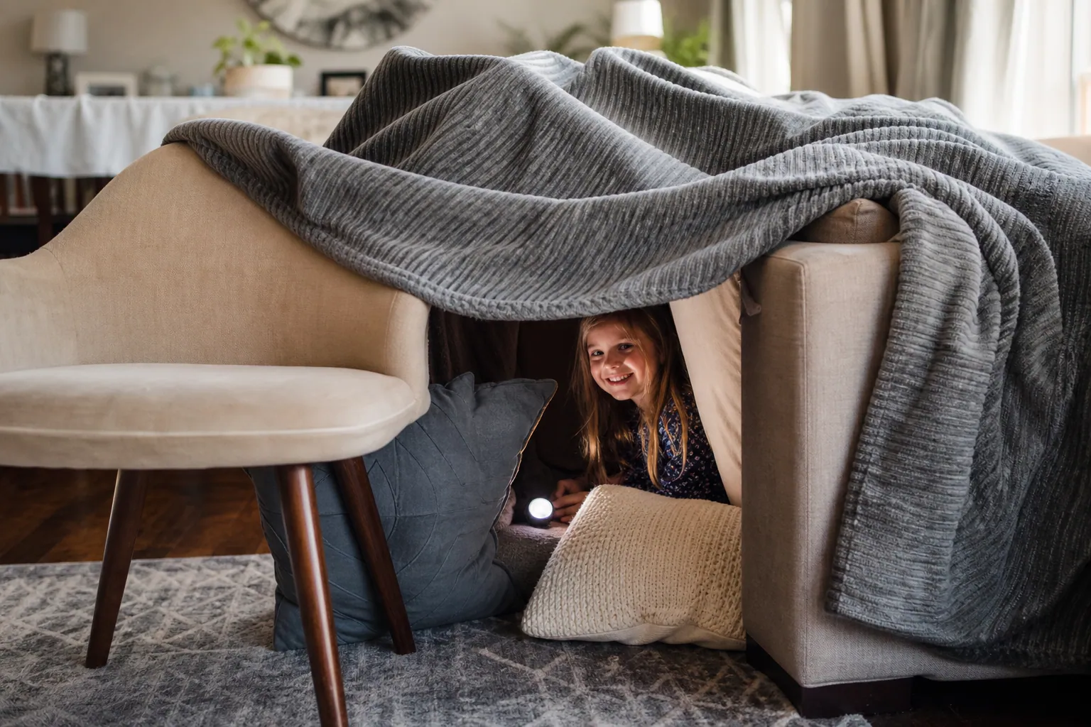 Un enfant sourit à l'intérieur d'une cabane construite avec des couvertures et des coussins.