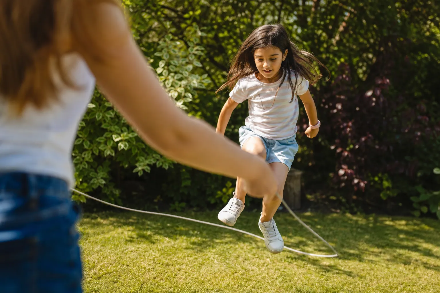 Un enfant saute par-dessus une corde à sauter dans un jardin ensoleillé.