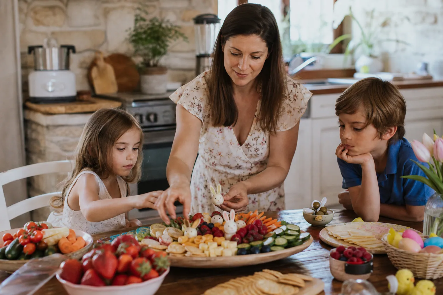 Parent et enfants préparant un plateau de collation de Pâques coloré dans la cuisine.