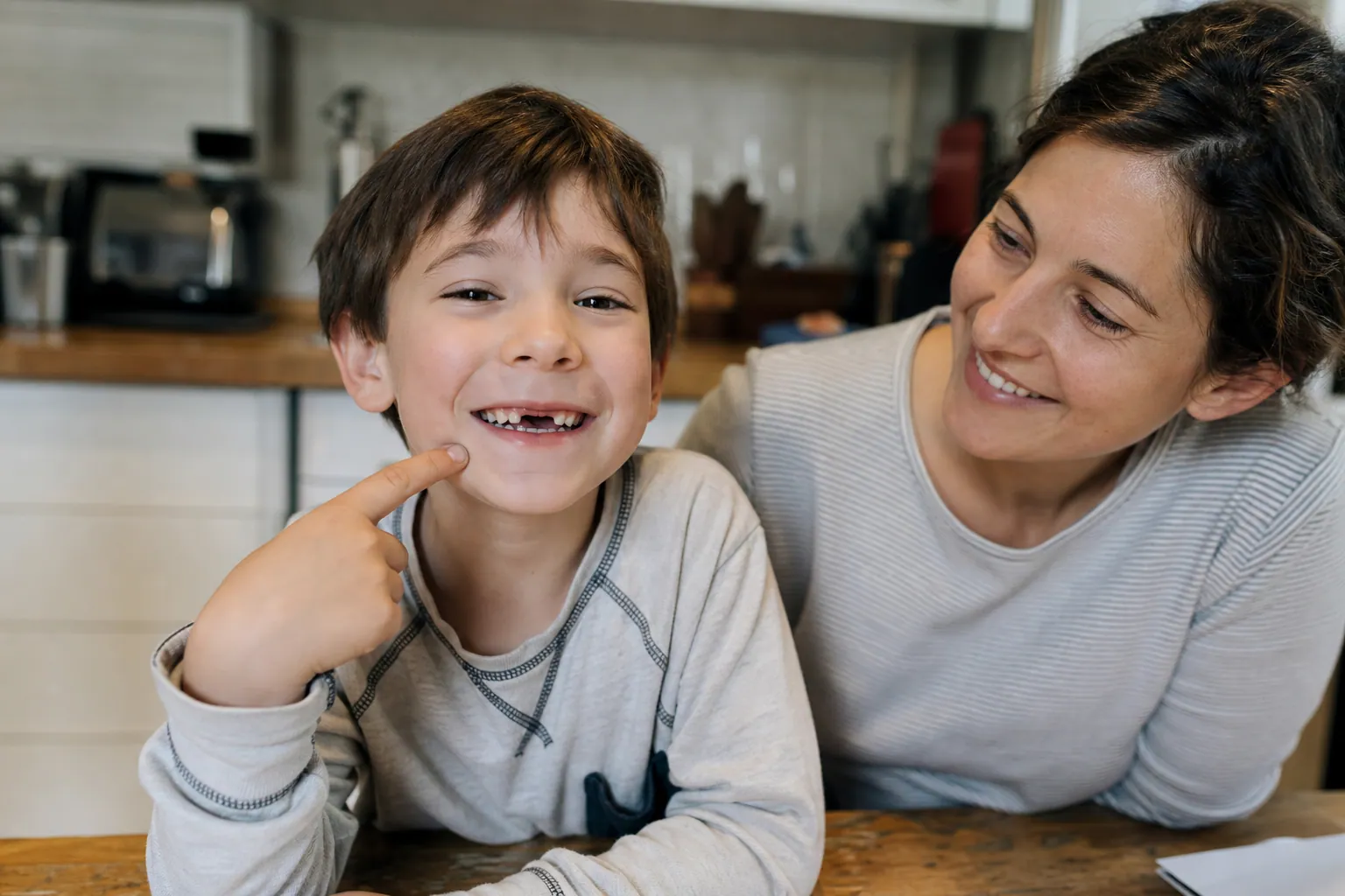 Un enfant sourit largement, une dent de lait manquante à l'avant, aux côtés d'un parent attendri.
