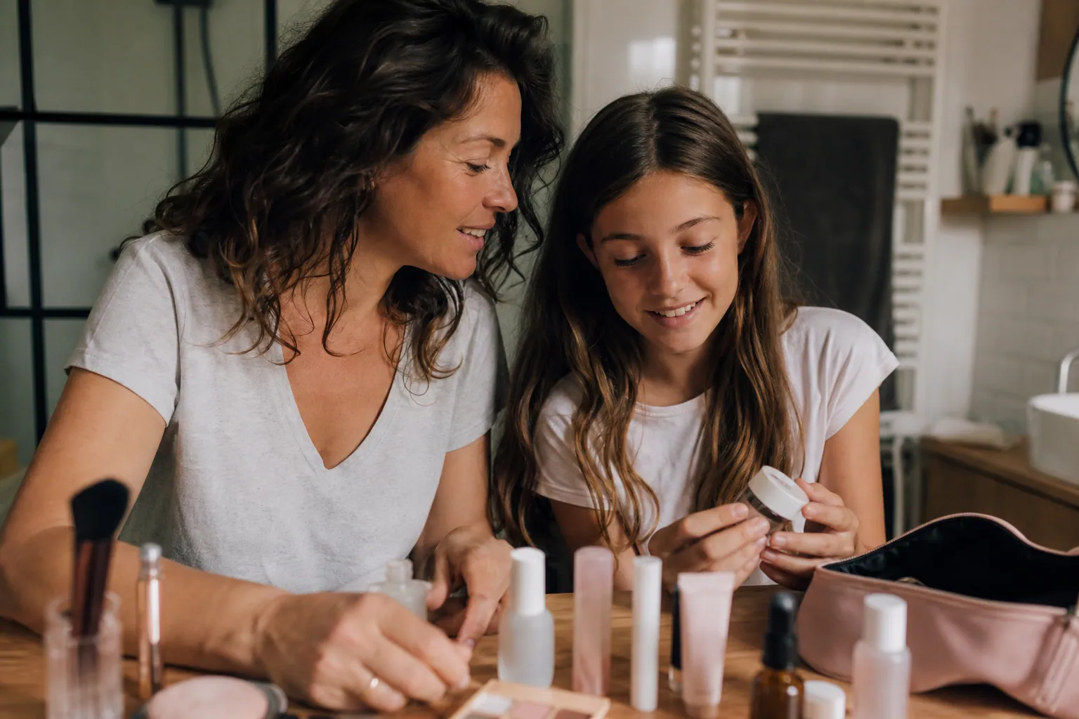 Mère et fille de 12 ans discutant d’un maquillage léger dans une salle de bain lumineuse.