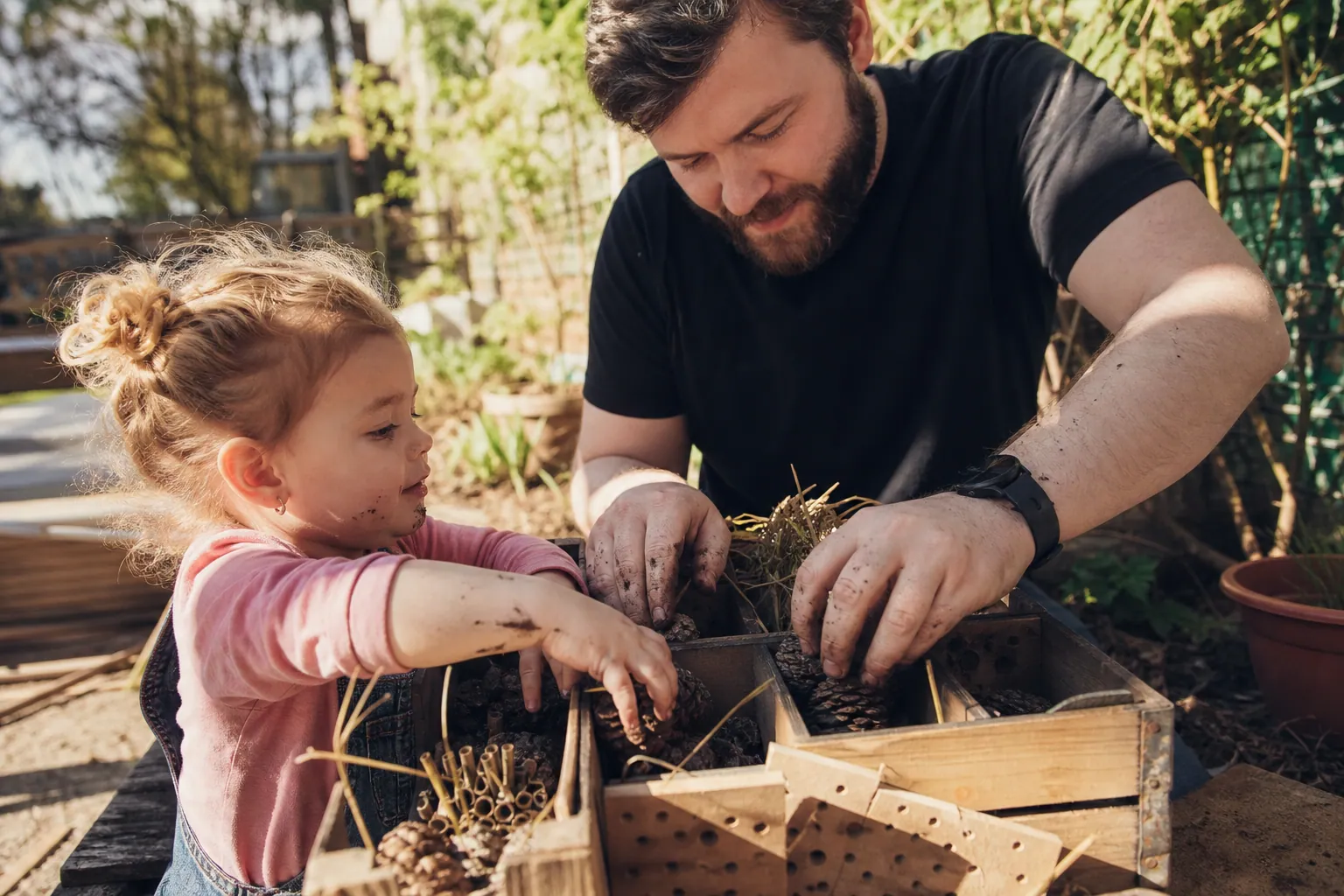 Un parent et son enfant fabriquent ensemble un hôtel à insectes en bois dans le jardin.