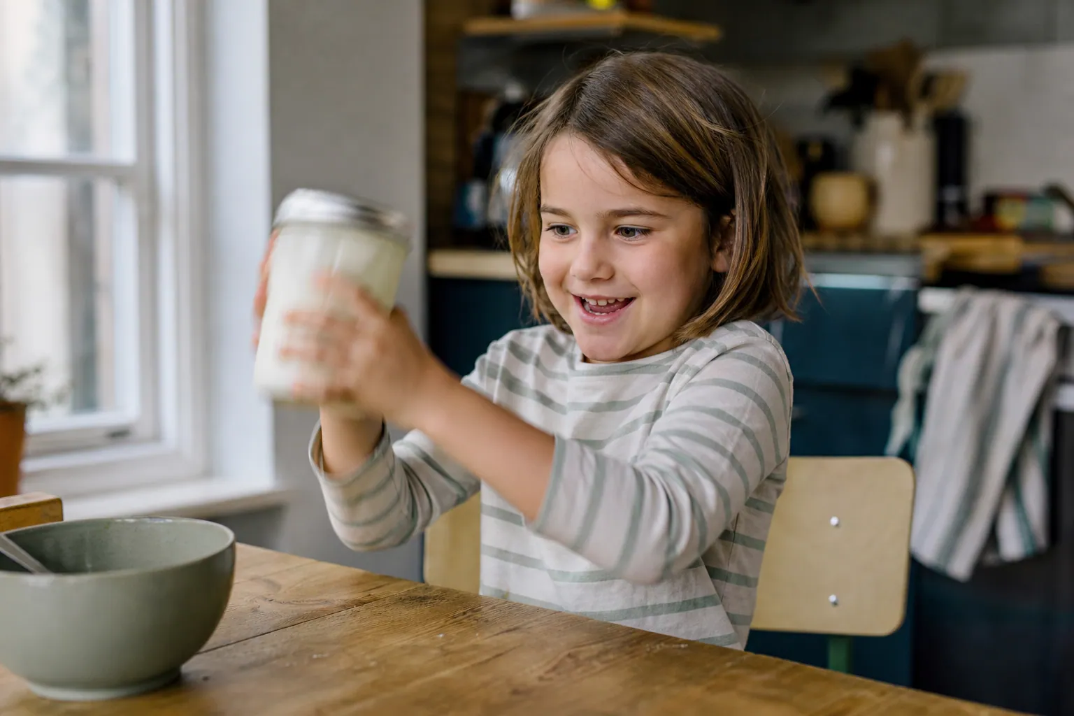 Un enfant secoue un bocal en verre rempli de crème pour fabriquer du beurre maison.