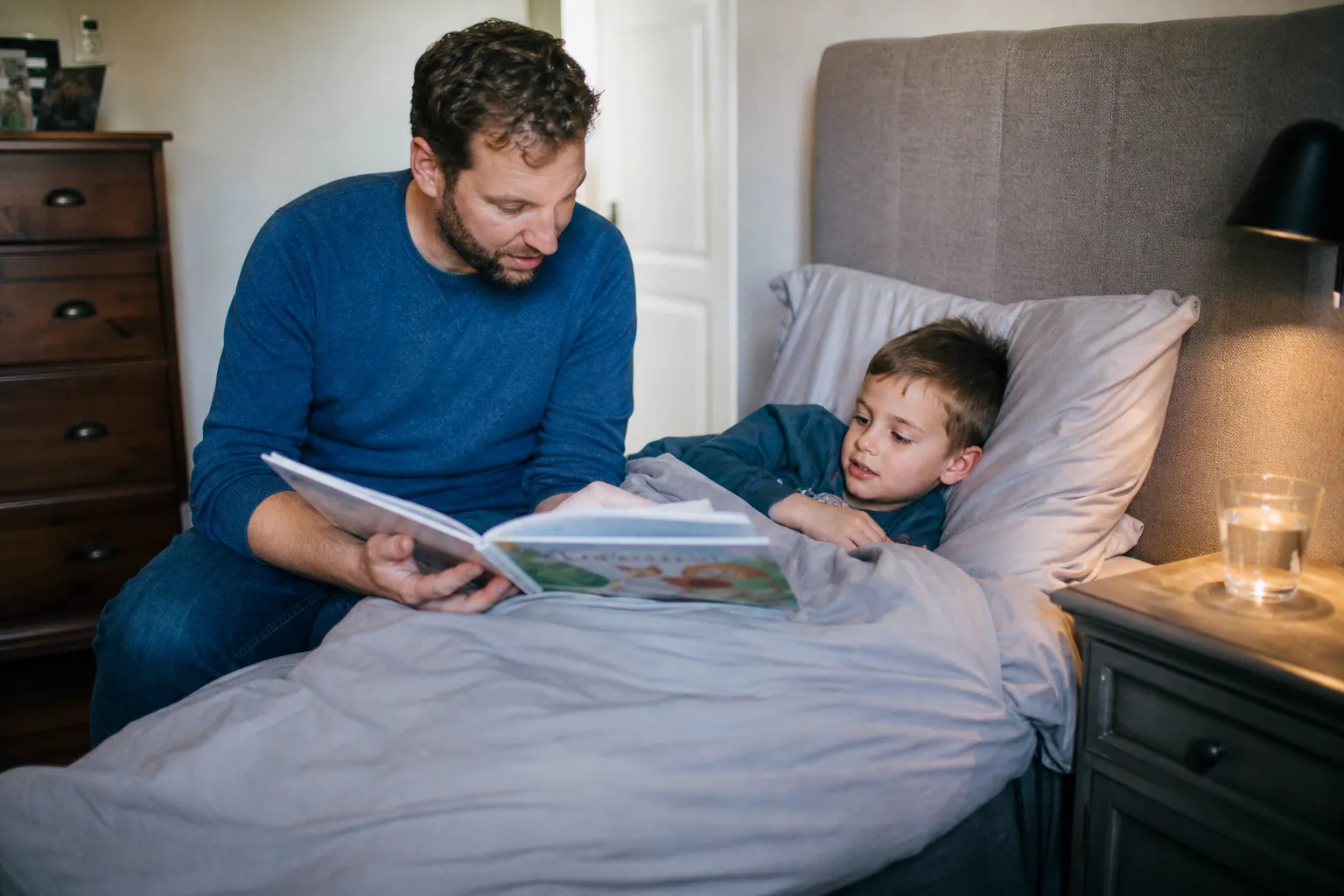 Un parent lit une histoire à son enfant au repos dans son lit, un verre d'eau à portée de main.