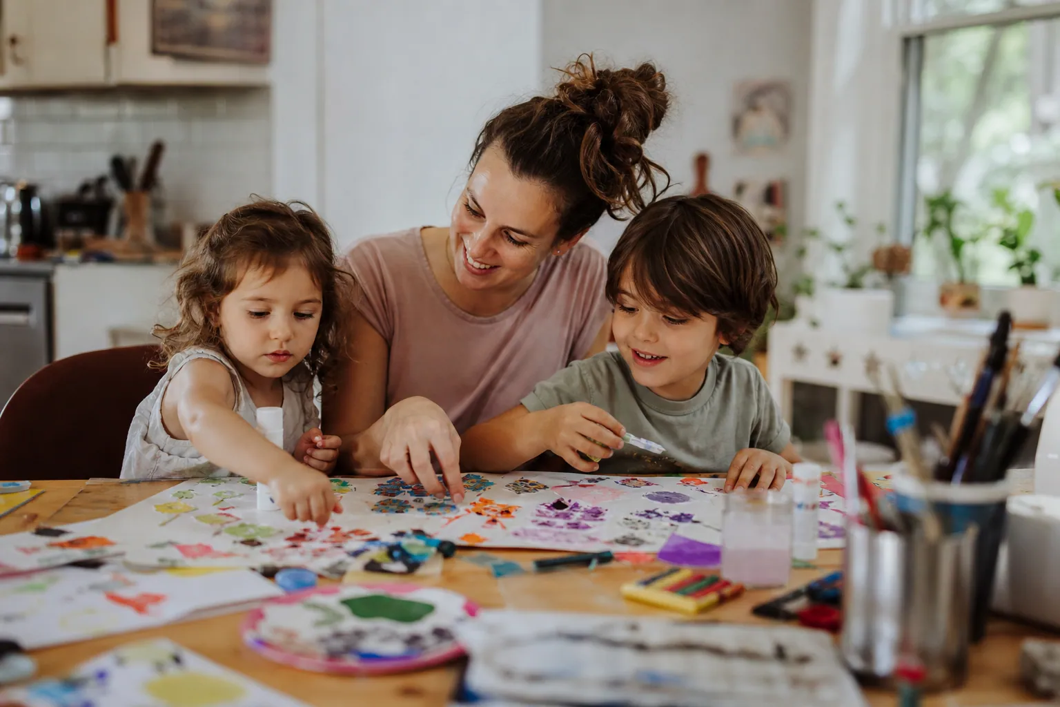 Parent et enfants réalisant un collage et de la peinture à table, dans une lumière douce.