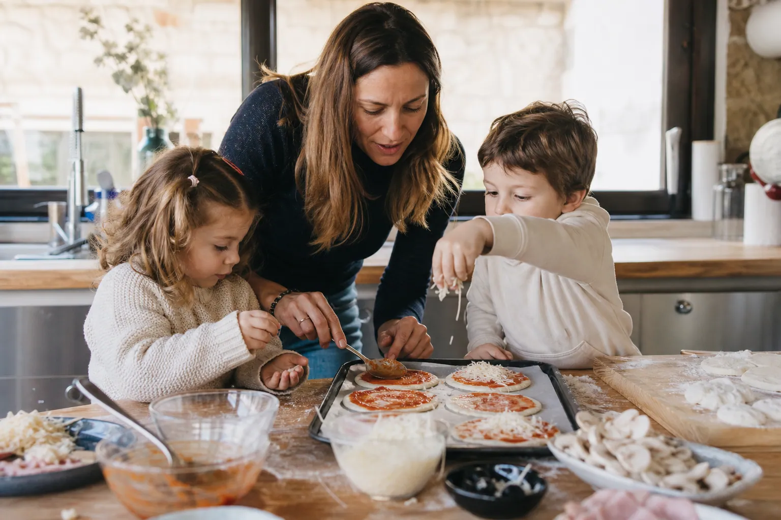 Parent et enfants préparant des mini pizzas dans une cuisine familiale lumineuse.