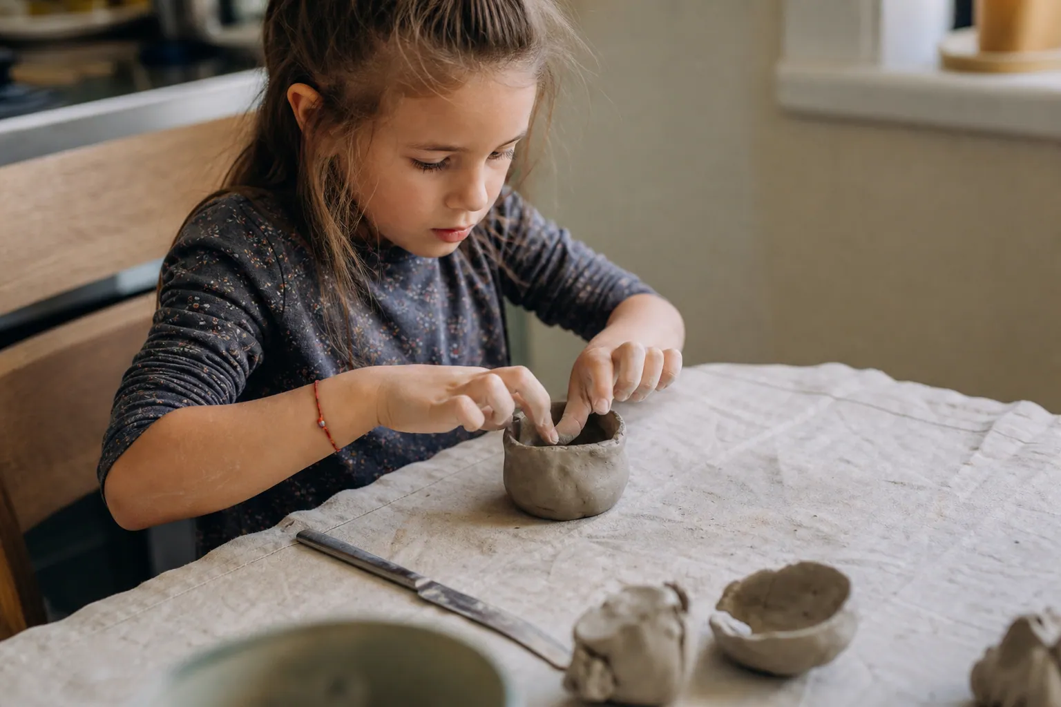 Un enfant façonne un petit bol en argile avec ses mains sur une table protégée.