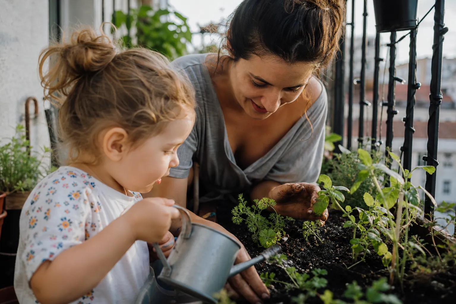 Parent et enfant jardinant ensemble sur un balcon avec de jeunes plants