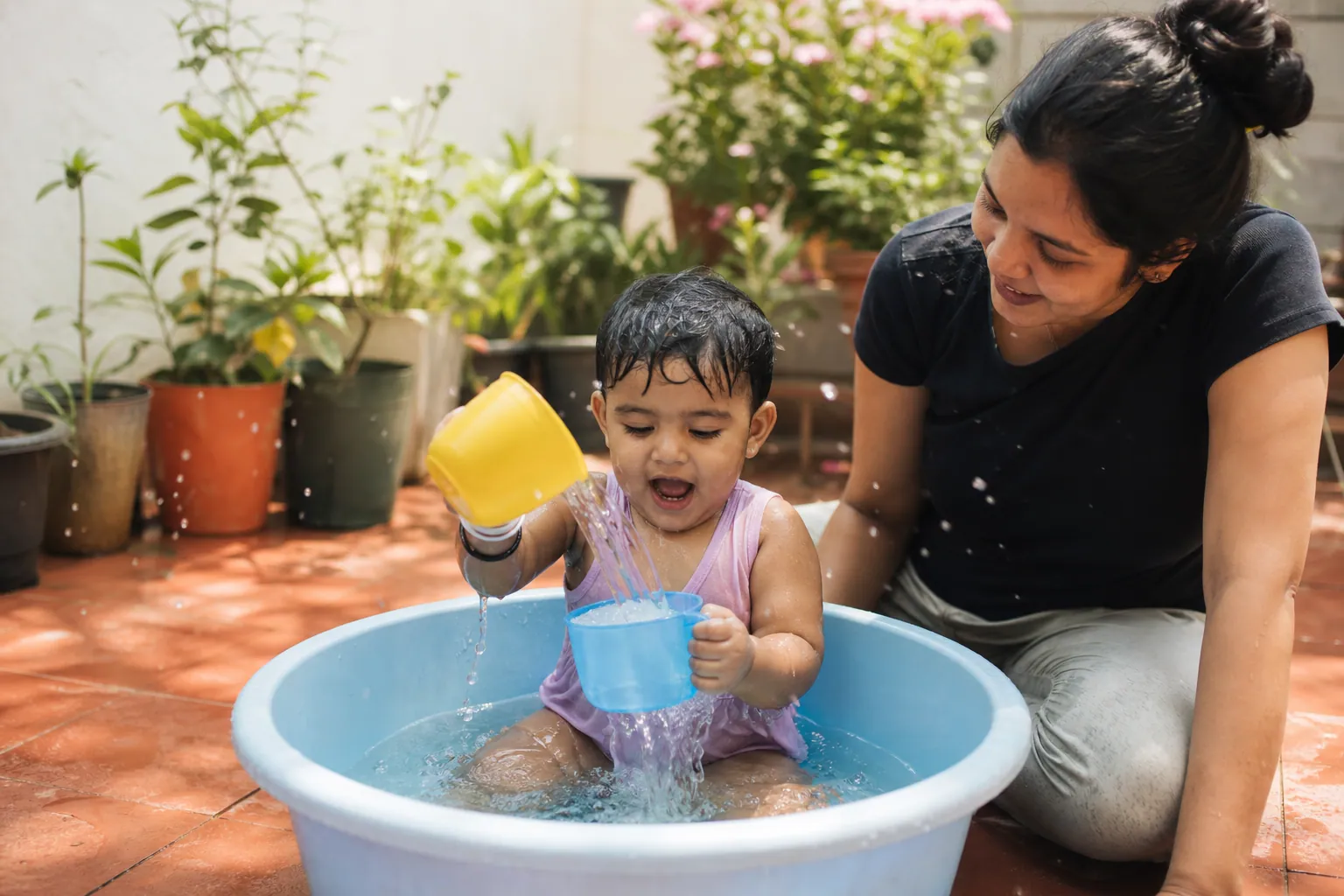 Un enfant joue avec de l'eau dans une bassine en plastique sur une terrasse ensoleillée