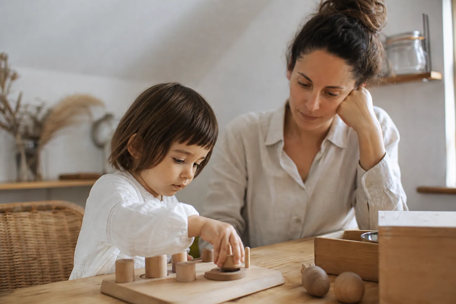 Enfant jouant avec un parent à un jeu Montessori en bois dans un intérieur chaleureux.