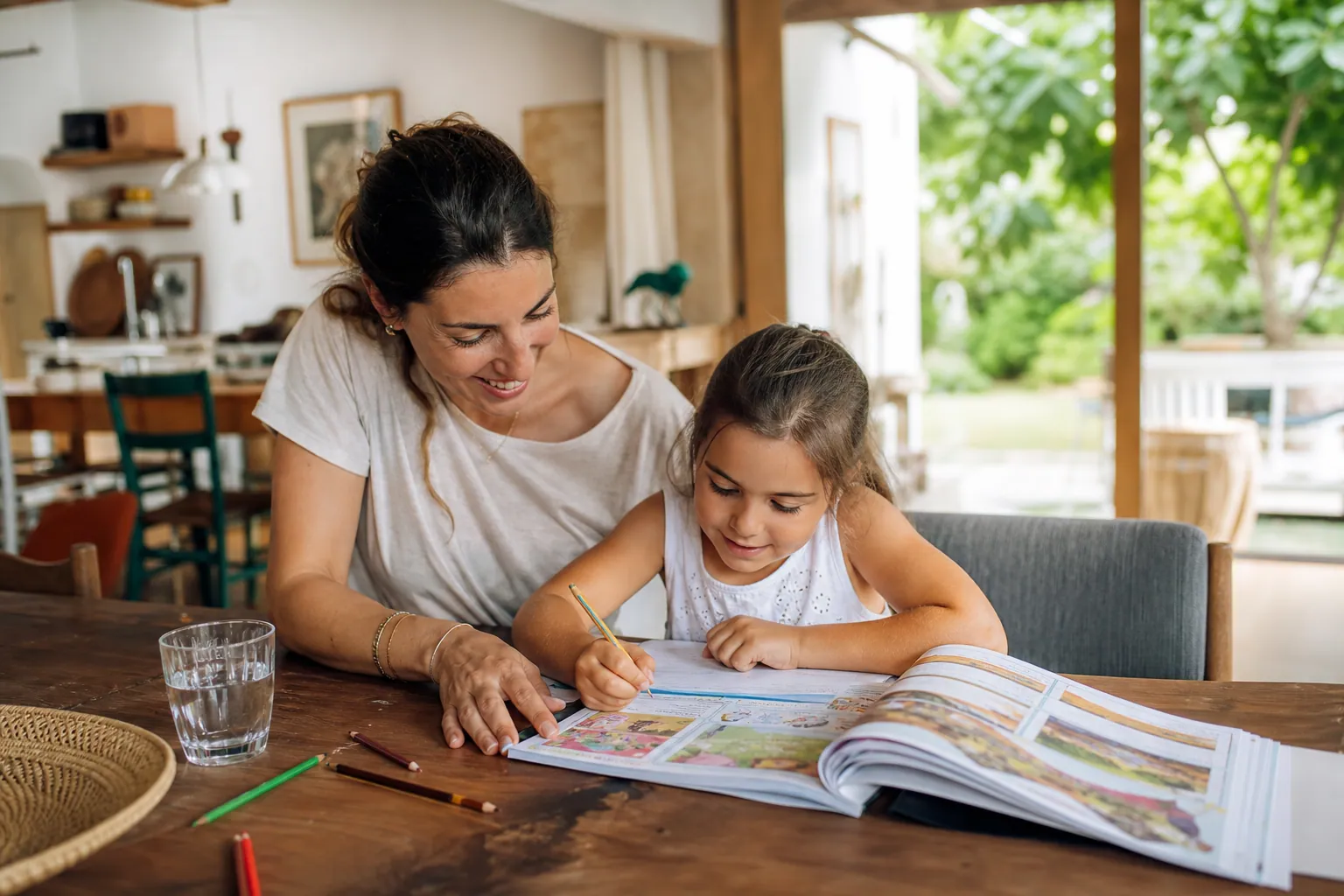 Parent et enfant de CP travaillant sur un cahier de vacances à la maison