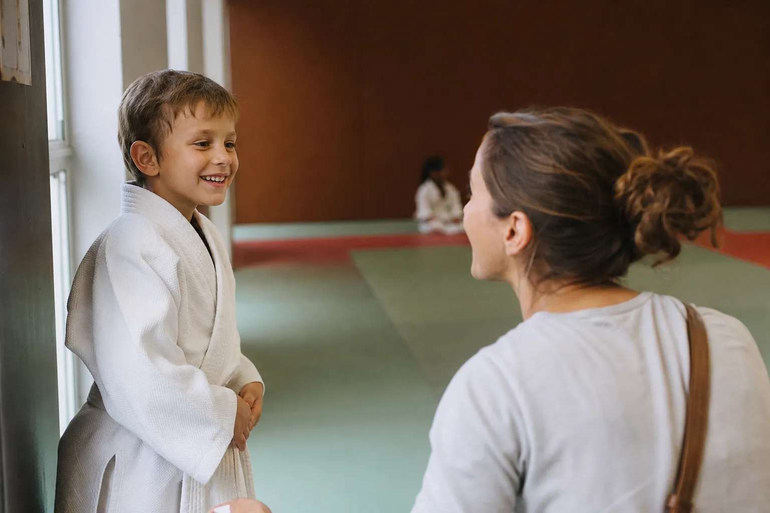 Parent français observant son enfant en tenue de judo dans un dojo lumineux.