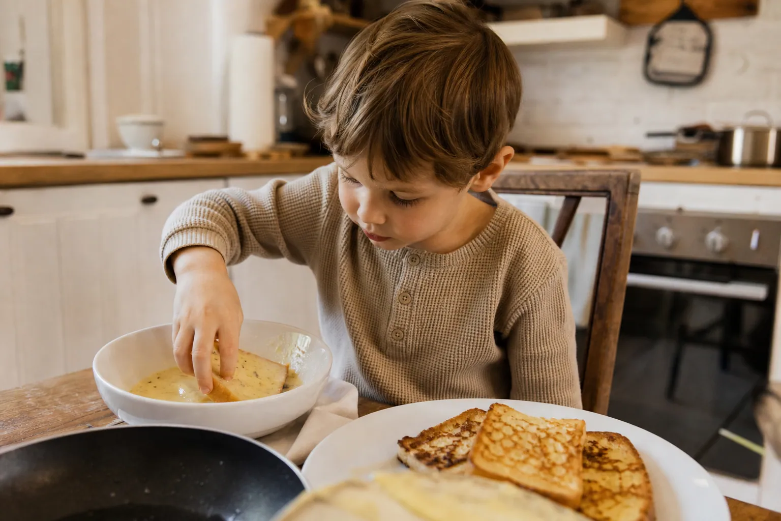 Un enfant trempe une tranche de pain dans un mélange d'œufs et de lait pour faire du pain perdu.