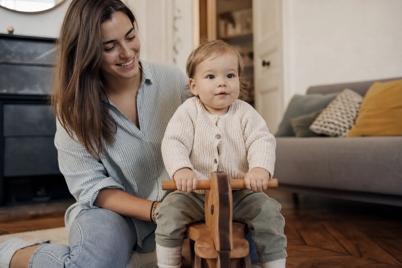 Un bébé de 1 an sur un porteur, surveillé par un parent dans un salon lumineux.