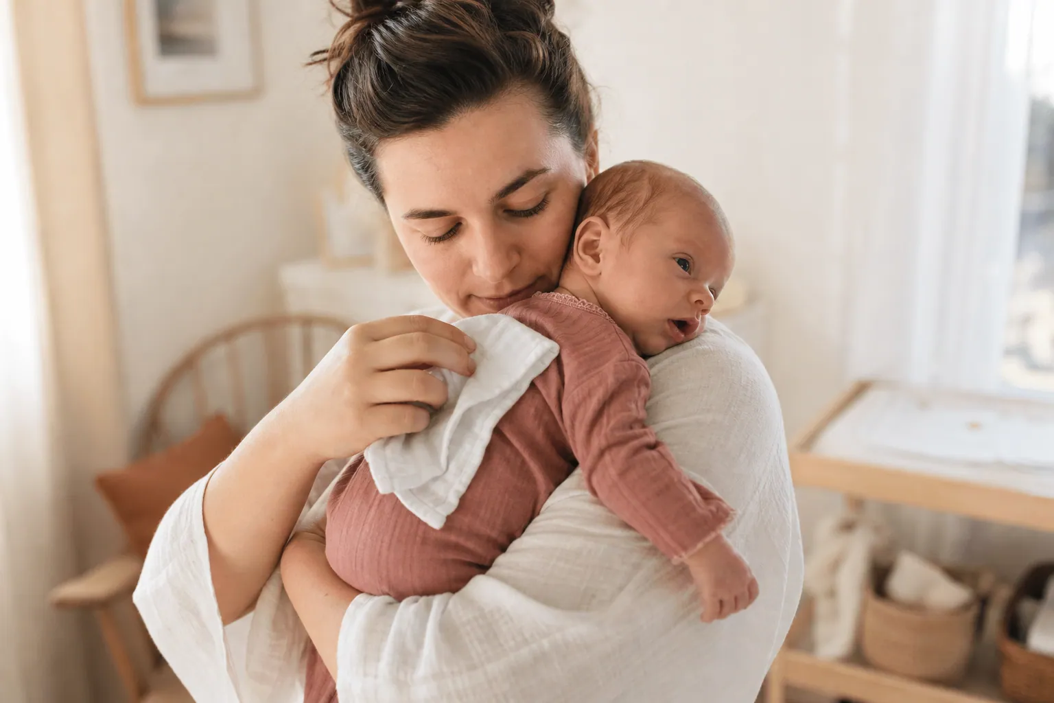 Parent tenant un nouveau-né avec un lange en coton doux dans une chambre lumineuse.