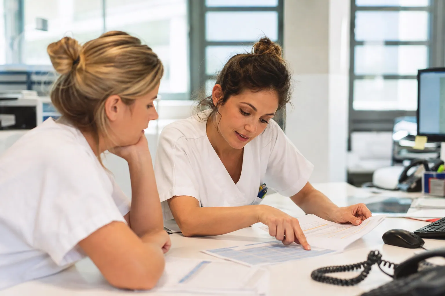 Infirmière française consultant son planning dans un hôpital, avec une collègue.