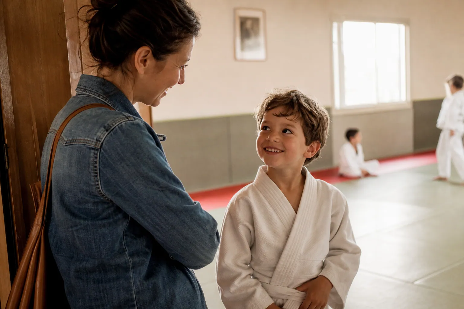 Un enfant en tenue de sport de combat avec son parent dans un dojo lumineux.