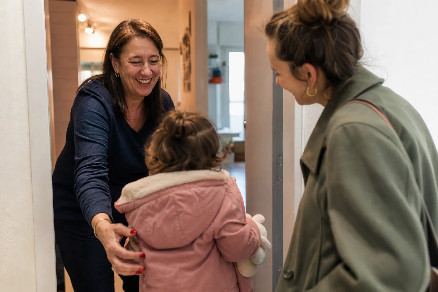 Assistante maternelle accueillant un jeune enfant avec un parent, en contexte chaleureux