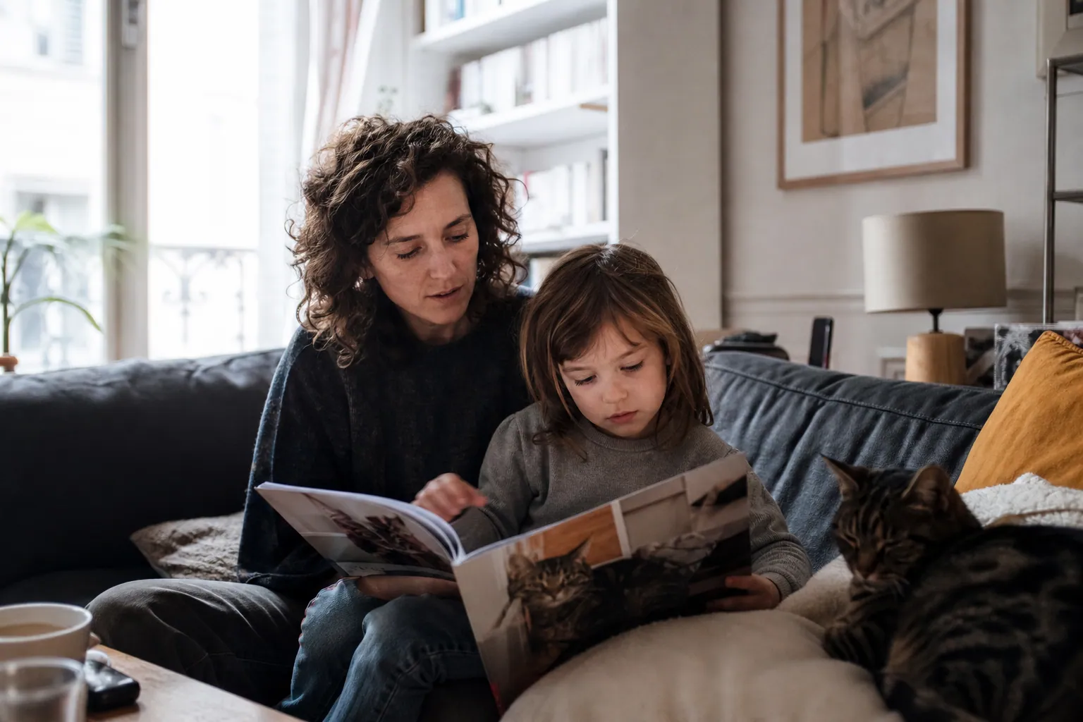 Parent et enfant lisant un magazine sur les chats avec un chat calme à leurs côtés.