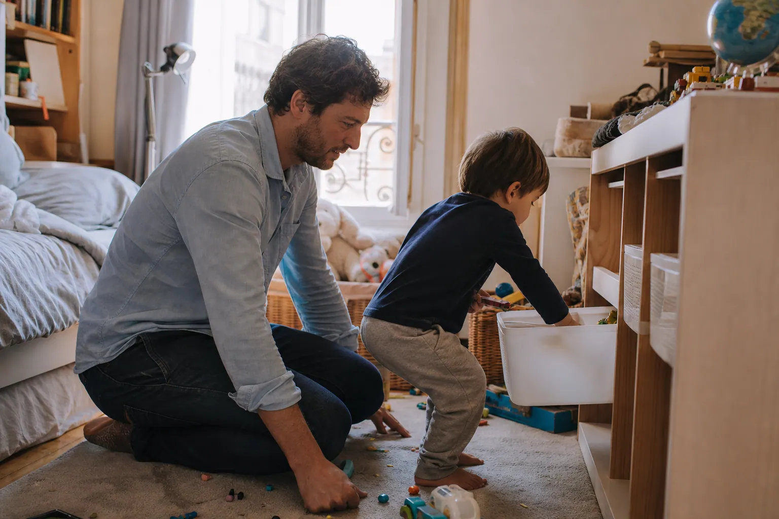 Parent aidant un enfant à ranger sa chambre avec des bacs colorés