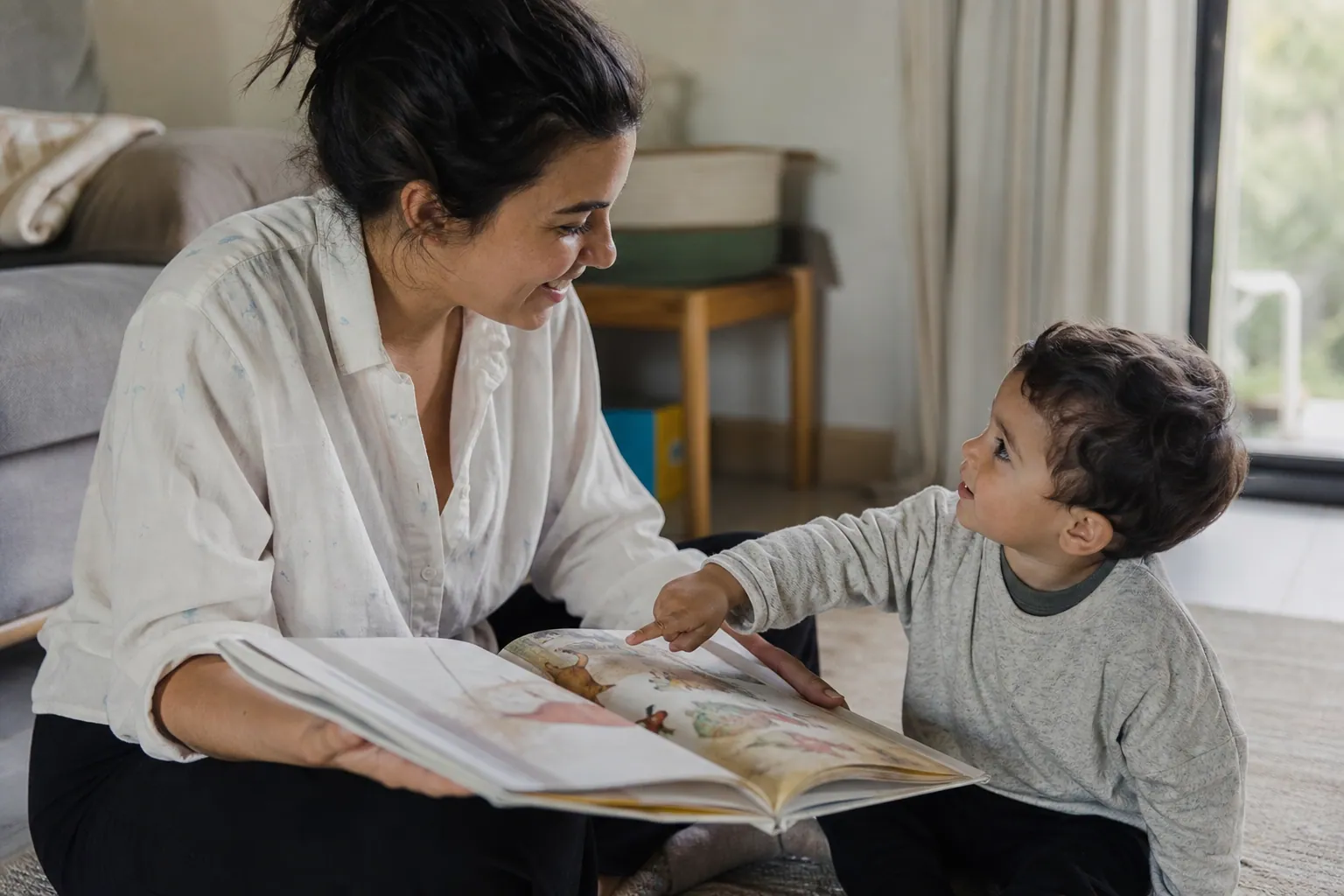 Un parent assis face à son tout-petit qui pointe une image dans un imagier ouvert entre eux.